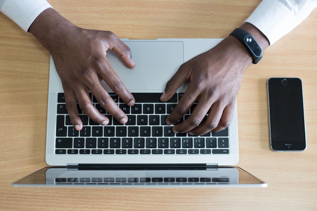 Foto tirada de cima de um homem mexendo no computador - vê-se apenas as mãos sobre o teclado.